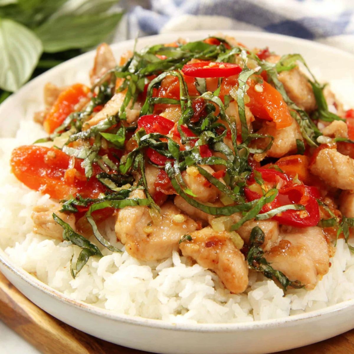 Creamy Thai basil chicken served over jasmine rice with basil leaves and chili on top,  on a white kitchen counter.