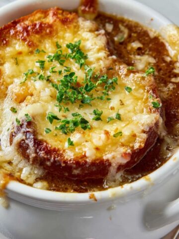 Featured image of crock pot French onion soup topped with melted cheese and bread, photographed from above on a white kitchen counter.