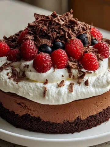 Homemade dark chocolate mousse cake with whipped cream and chocolate shavings, on a kitchen counter.