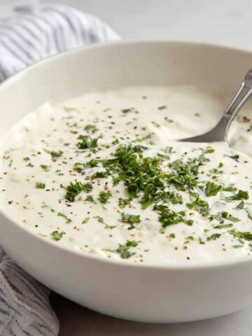 A bowl of Creamy healthy alfredo sauce recipe with parsley garnish on a white counter.