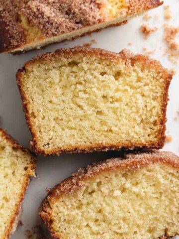 Freshly baked cinnamon donut bread loaf with slices and cinnamon sugar topping on a white counter.