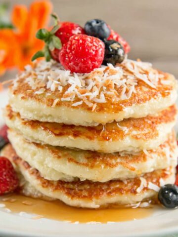 Stack of fluffy coconut cream pancakes topped with toasted coconut and berries