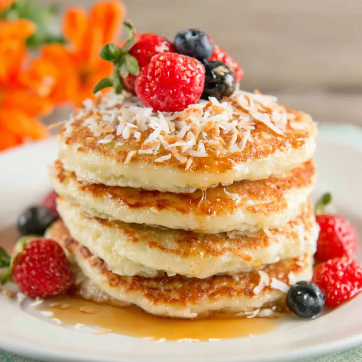 Stack of fluffy coconut cream pancakes topped with toasted coconut and berries