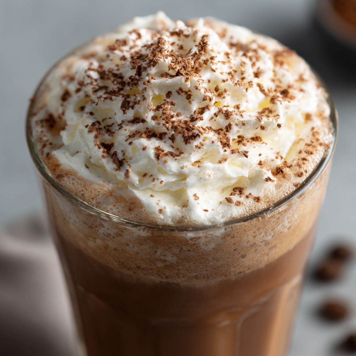 Glass of mocha iced coffee topped with whipped cream and chocolate on a white kitchen counter

