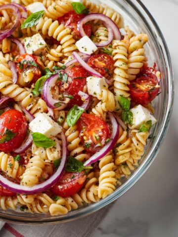 Tomato basil pasta salad in a bowl with fresh basil and cherry tomatoes on a white kitchen counter
