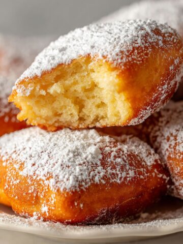 Homemade French beignets recipe dusted with powdered sugar on a white kitchen counter