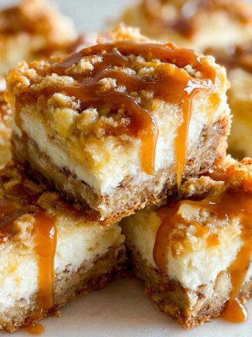 Homemade caramel apple cheesecake bars with caramel drizzle on white kitchen counter, top-down view