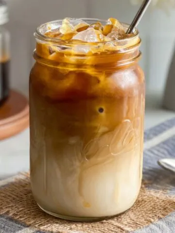 Homemade caramel iced coffee with whipped cream and caramel drizzle on a white kitchen counter