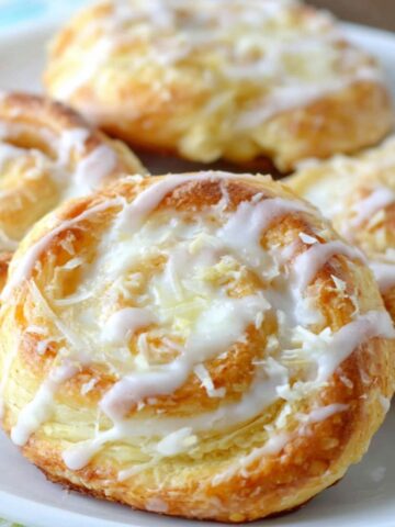 Freshly baked homemade cream cheese danish rolls on a white kitchen counter with glaze drizzled on top.