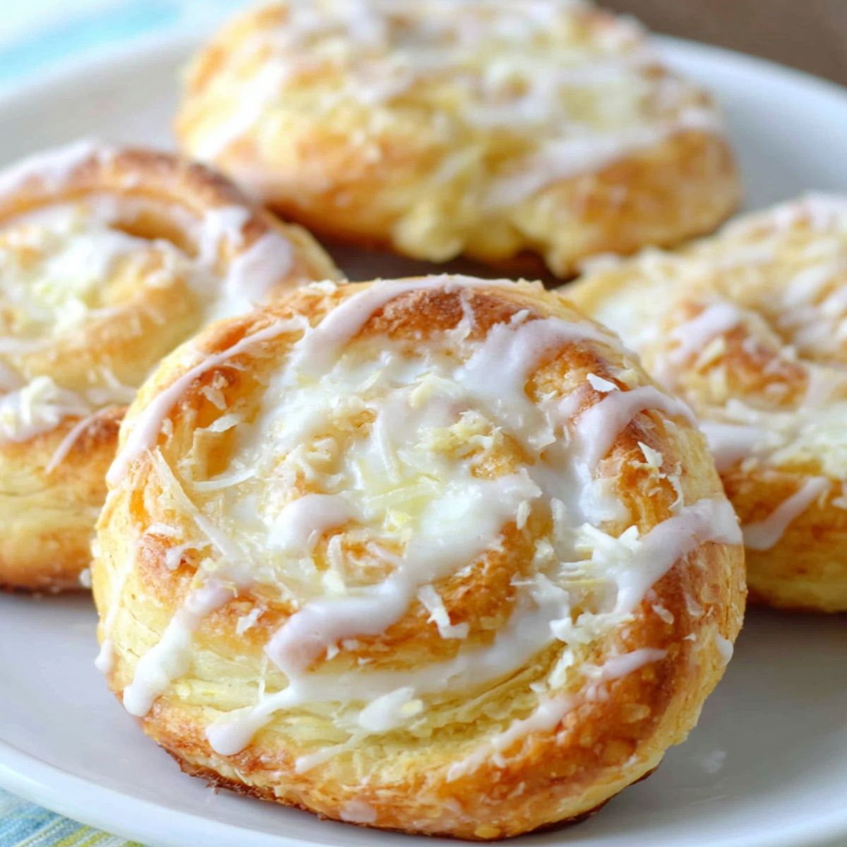 Freshly baked homemade cream cheese danish rolls on a white kitchen counter with glaze drizzled on top.