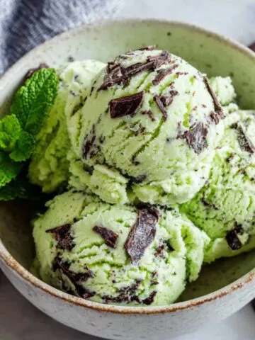 Homemade green mint chocolate chip ice cream with chocolate chunks in a ceramic bowl on a white kitchen counter.
