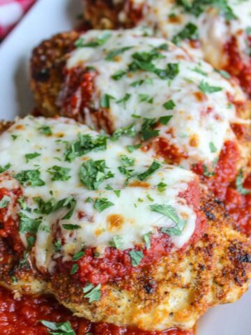 Homemade keto chicken parmesan on a white counter with melted mozzarella and marinara sauce, photographed from above.
