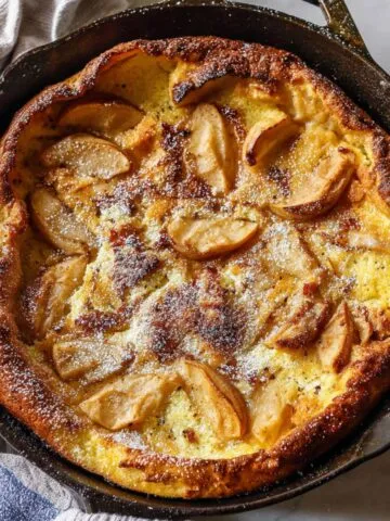 Overhead shot of a golden Dutch apple pancake fresh from the oven in a skillet on a kitchen counter