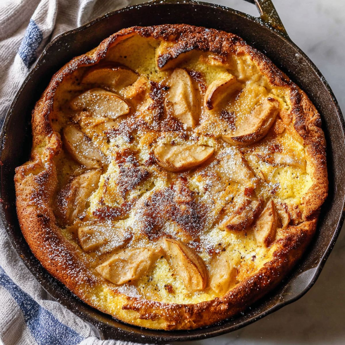 Overhead shot of a golden Dutch apple pancake fresh from the oven in a skillet on a kitchen counter