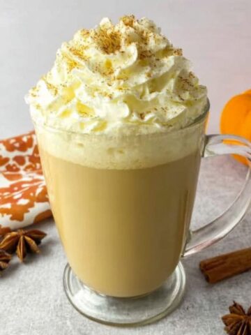 homemade pumpkin spice latte with whipped cream and cinnamon on a white kitchen counter.