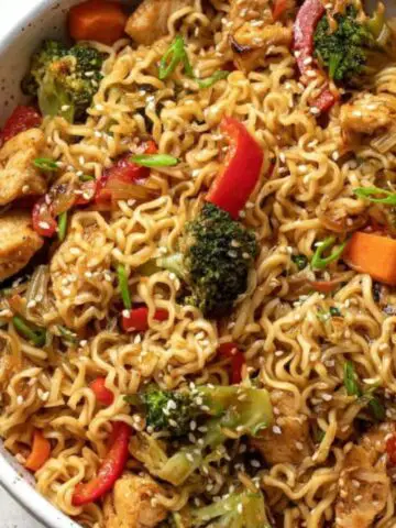 Homemade chicken ramen stir fry in a bowl with chicken, noodles, and vegetables on a white kitchen counter