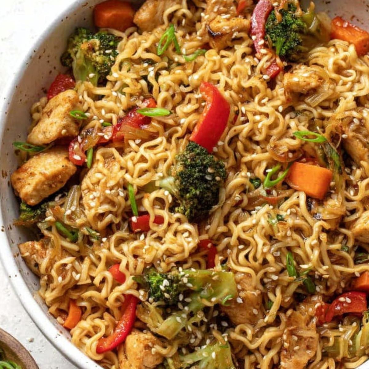 Homemade chicken ramen stir fry in a bowl with chicken, noodles, and vegetables on a white kitchen counter