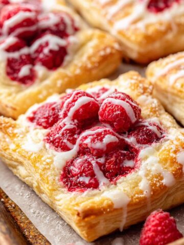 Freshly baked raspberry cream cheese danish pastries cooling on a white kitchen counter.