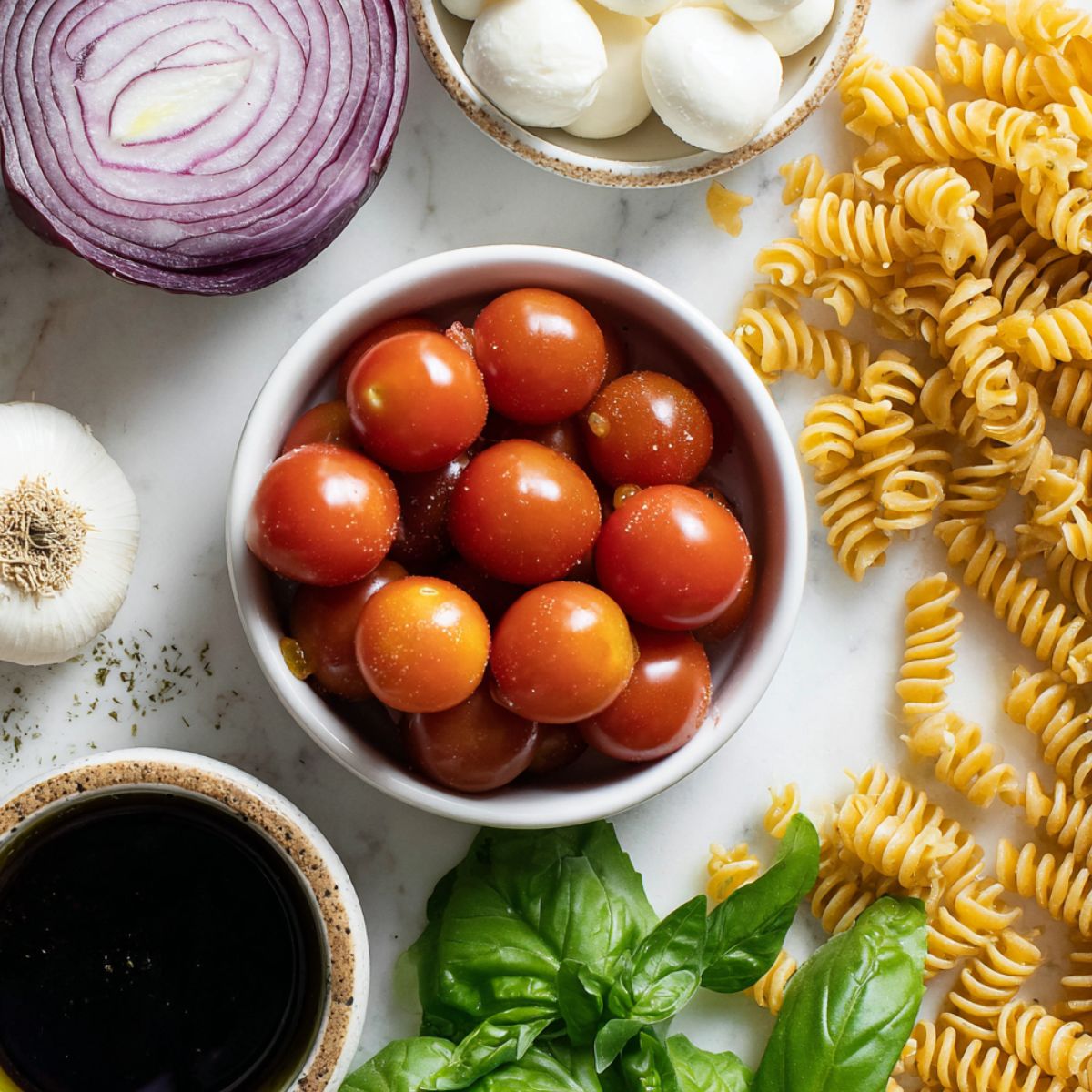 Ingredients for tomato basil pasta salad laid out casually on a white kitchen counter