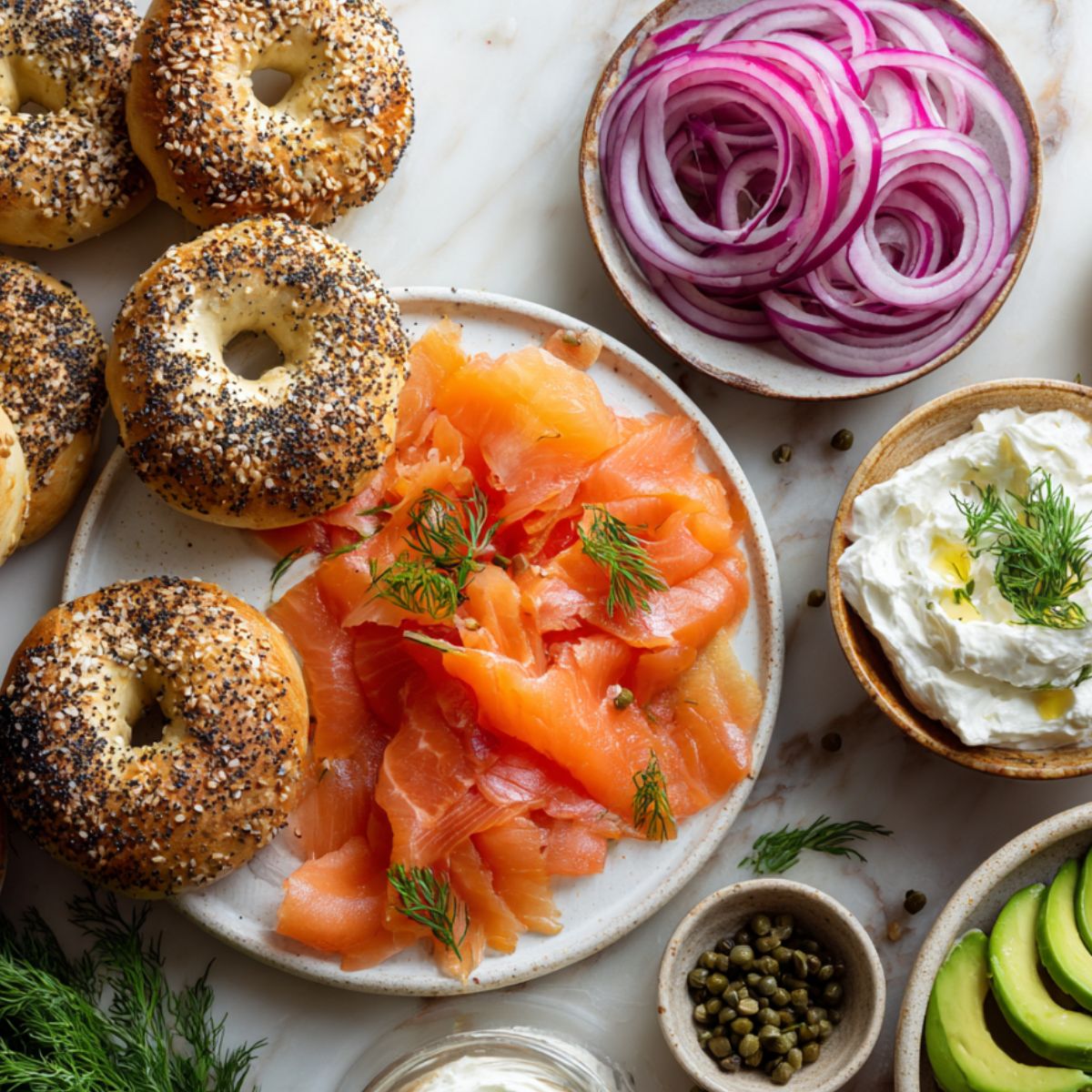 Top-down view of ingredients for a homemade salmon cream cheese bagel on a white kitchen counter.