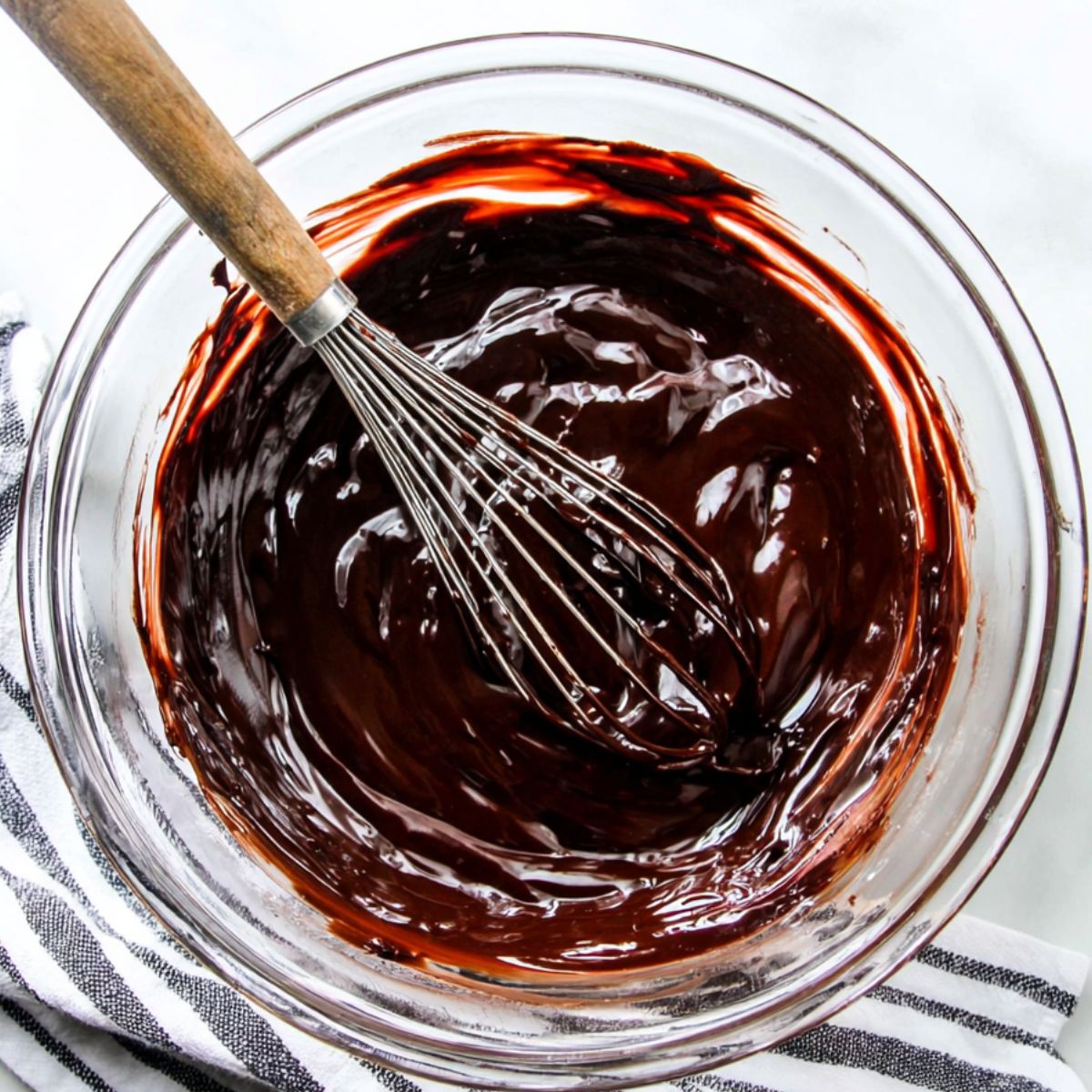 Melted chocolate in a glass bowl with a spatula on a kitchen counter