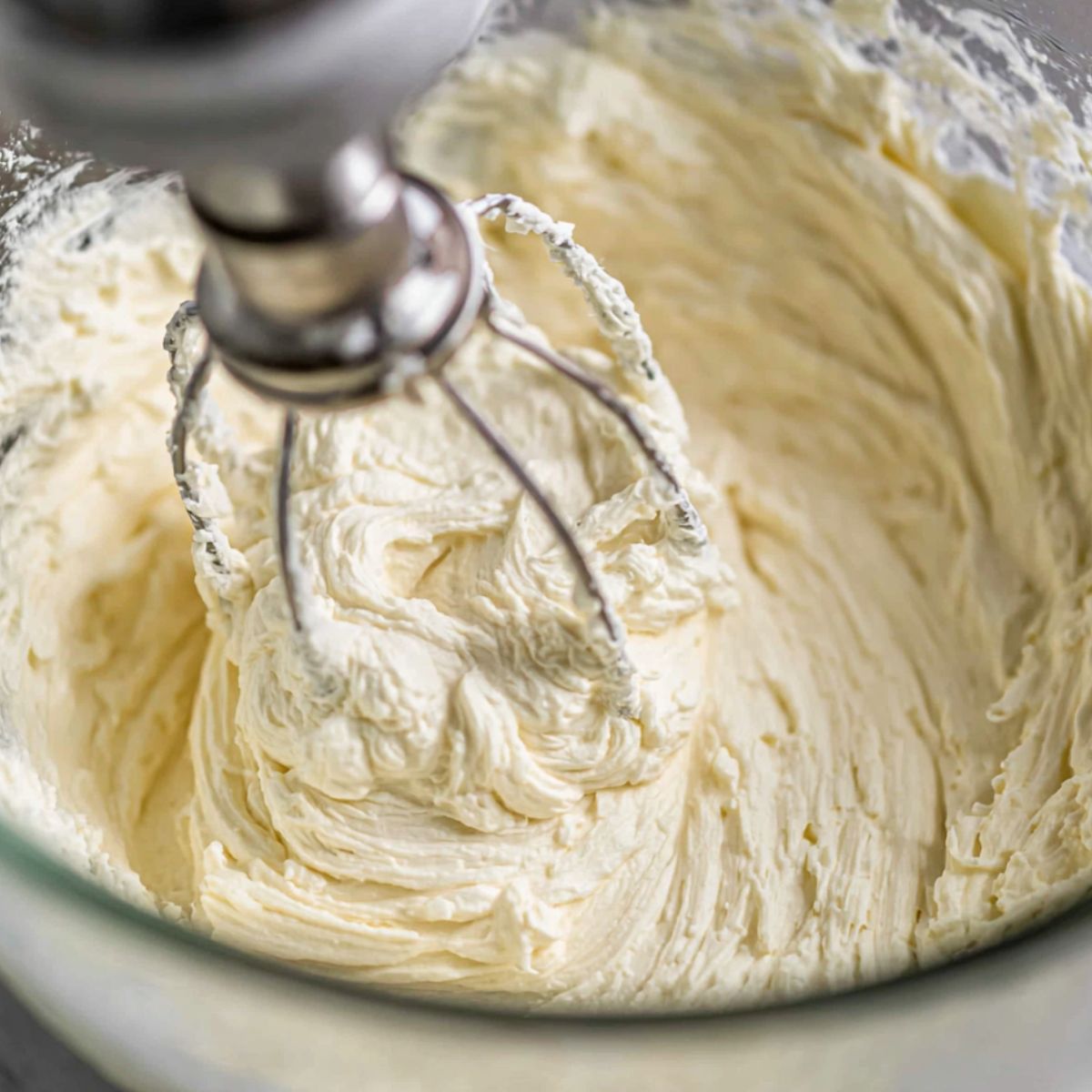 Cream cheese, powdered sugar, and vanilla being mixed in a bowl, viewed from above.