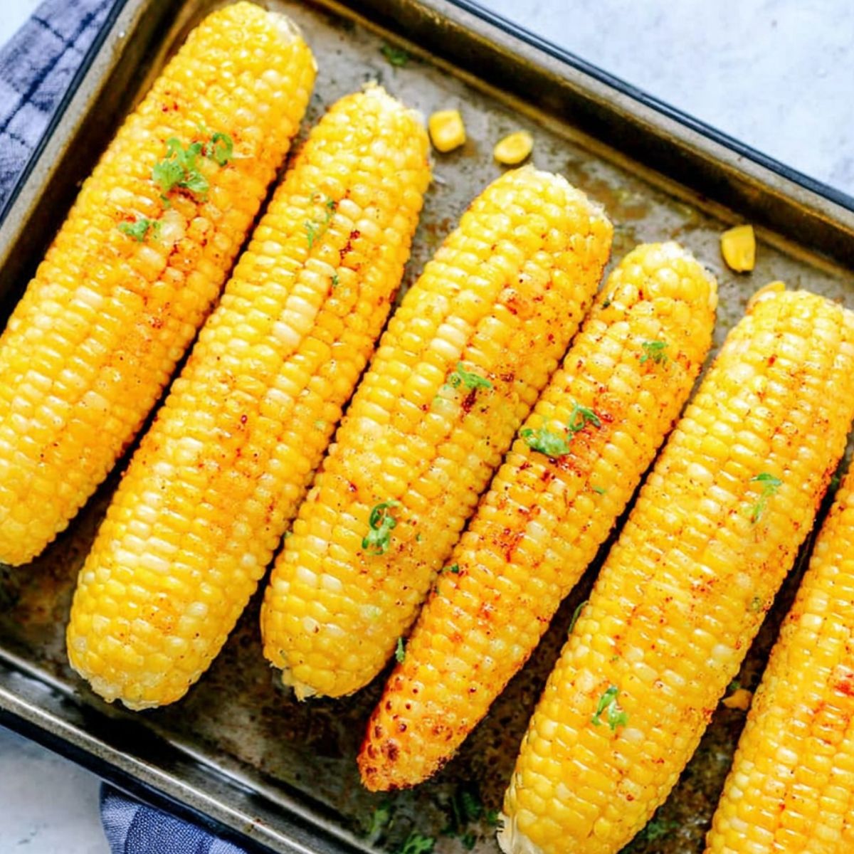 Fresh corn roasting in a home oven until golden and charred.