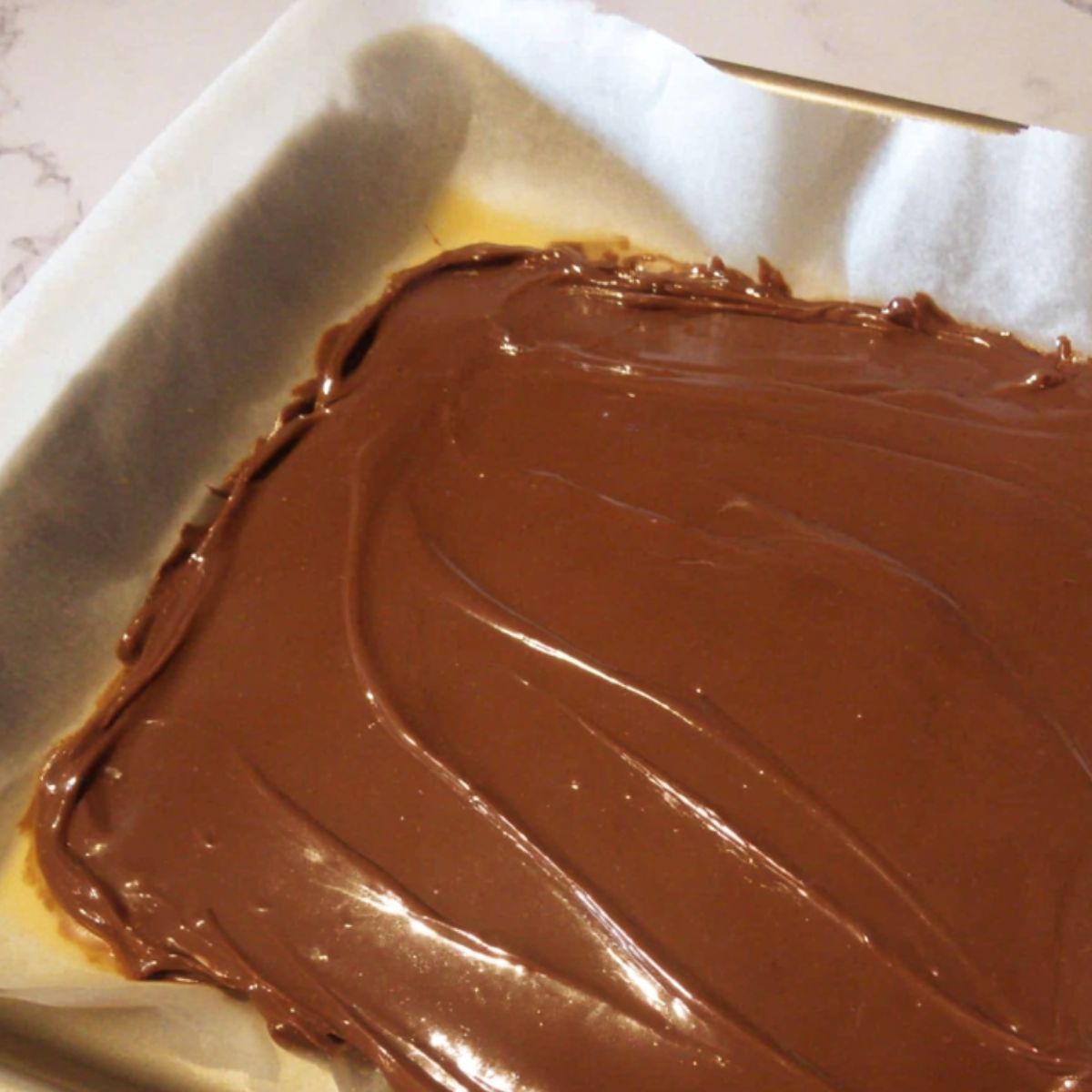 Spatula spreading melted chocolate on parchment paper for bark