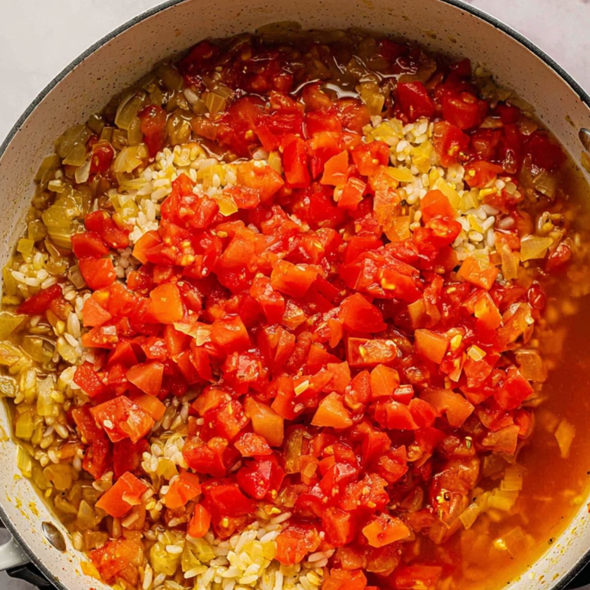 Rice, onion, and tomato simmering in a pan with broth