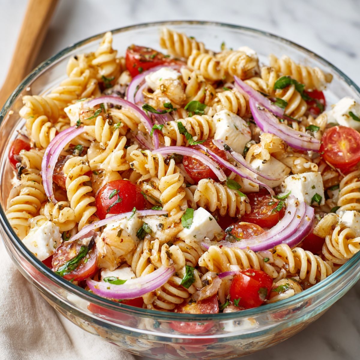 Tomato basil pasta salad being tossed in a mixing bowl