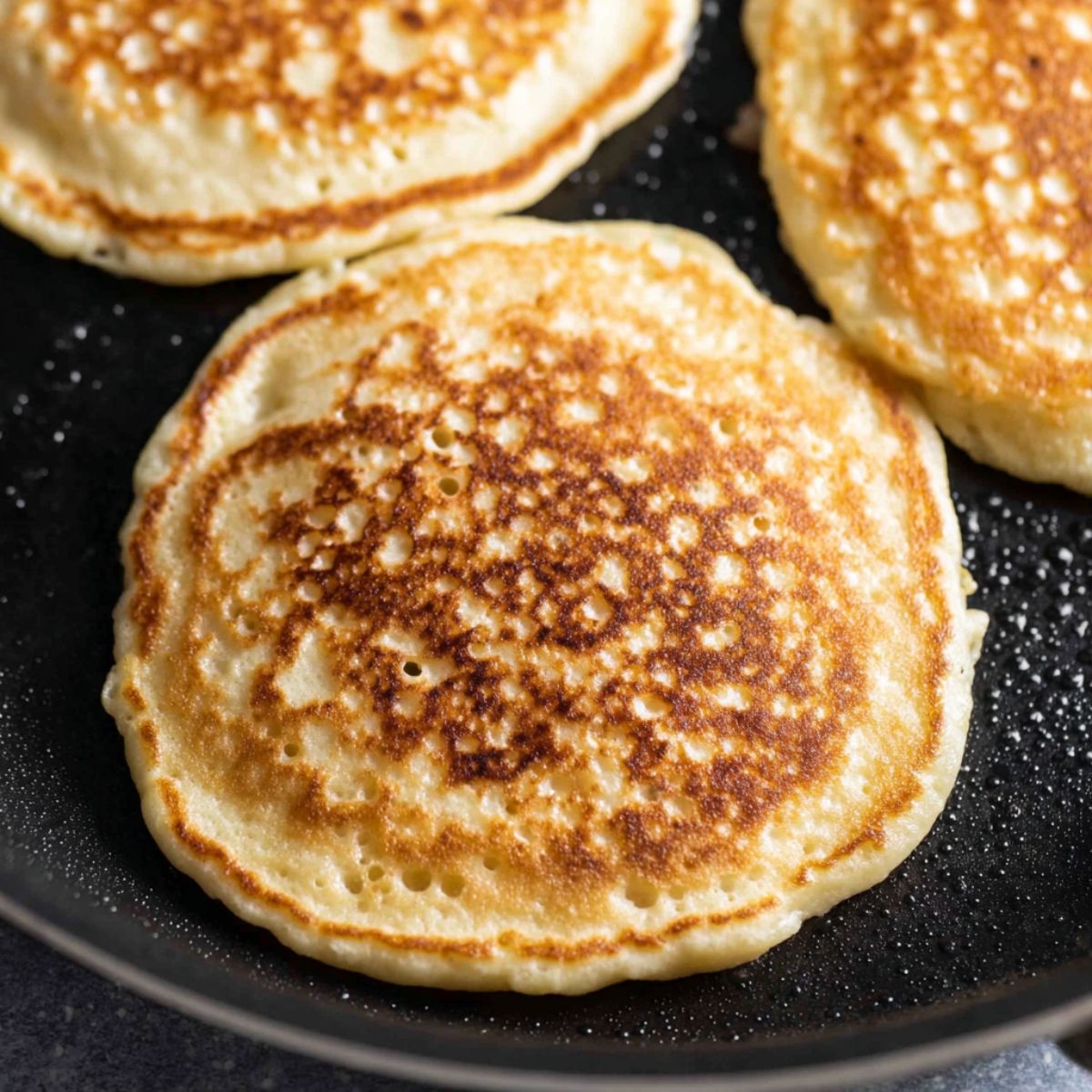 Pancakes cooking in a non-stick pan with bubbles forming on top