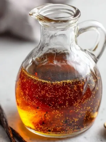 Homemade Vanilla Syrup Recipe for Coffee in a glass bottle next to a fresh cup of coffee on a white counter.