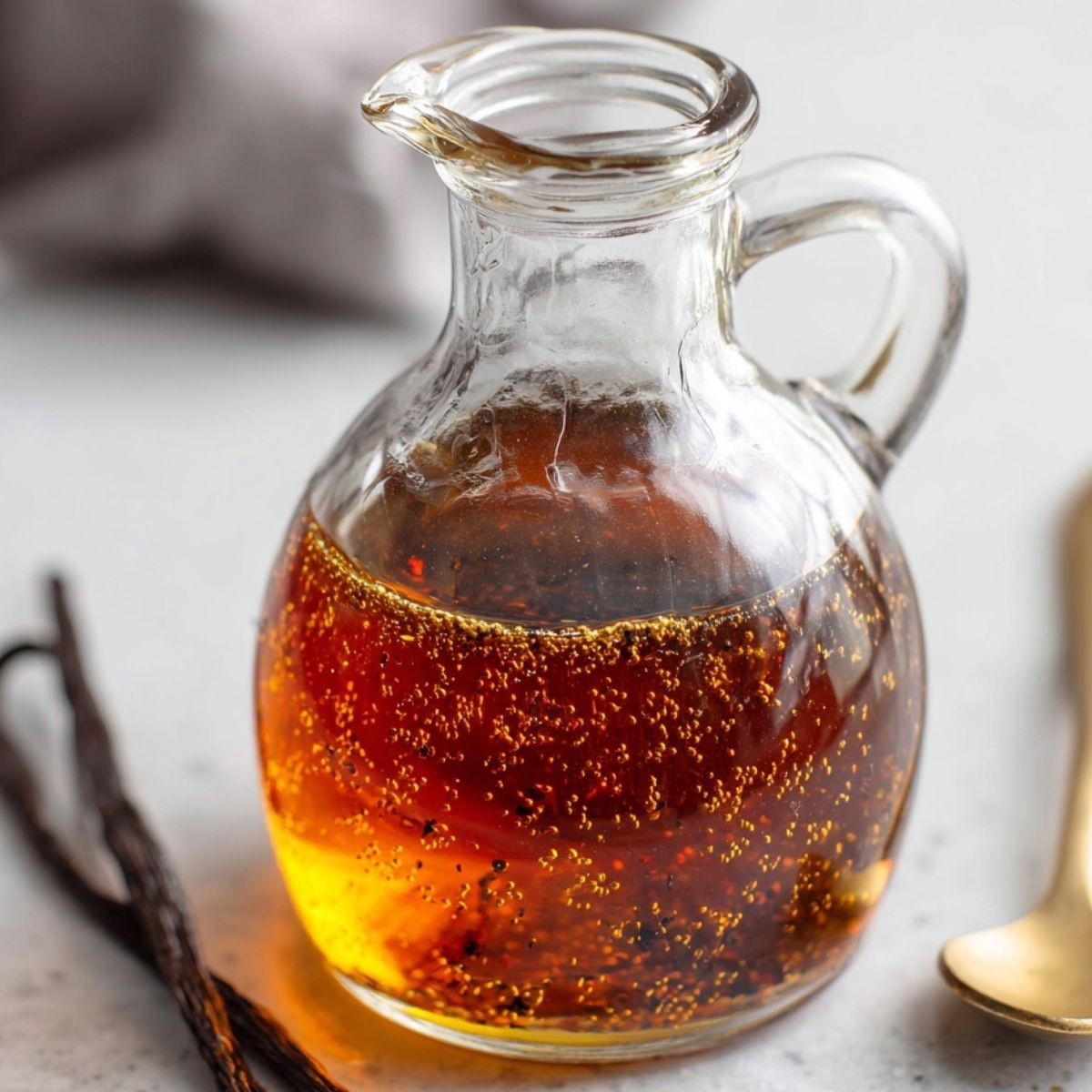 Homemade Vanilla Syrup Recipe for Coffee in a glass bottle next to a fresh cup of coffee on a white counter.