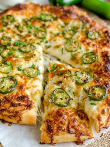 Overhead photo of a homemade jalapeño popper pizza with melted cheese, bacon, and sliced jalapeños.