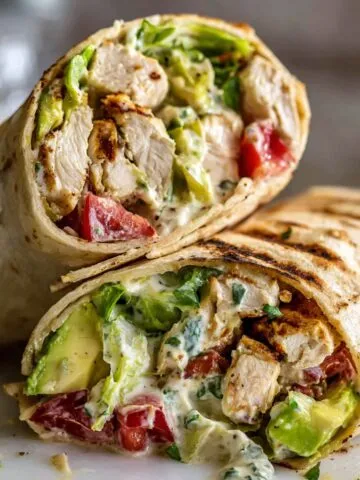 Overhead shot of a sliced homemade chicken avocado wrap on a white kitchen counter