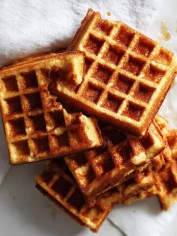 Stack of homemade cornbread waffles on a white kitchen counter with a rustic, cozy feel.