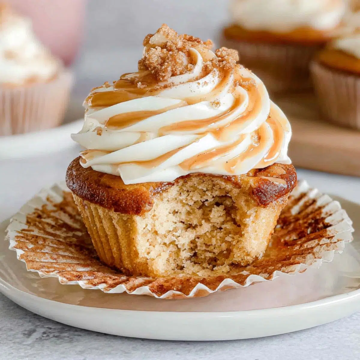 Homemade cinnamon roll cupcakes on a white counter, with imperfect frosting and a half-eaten one