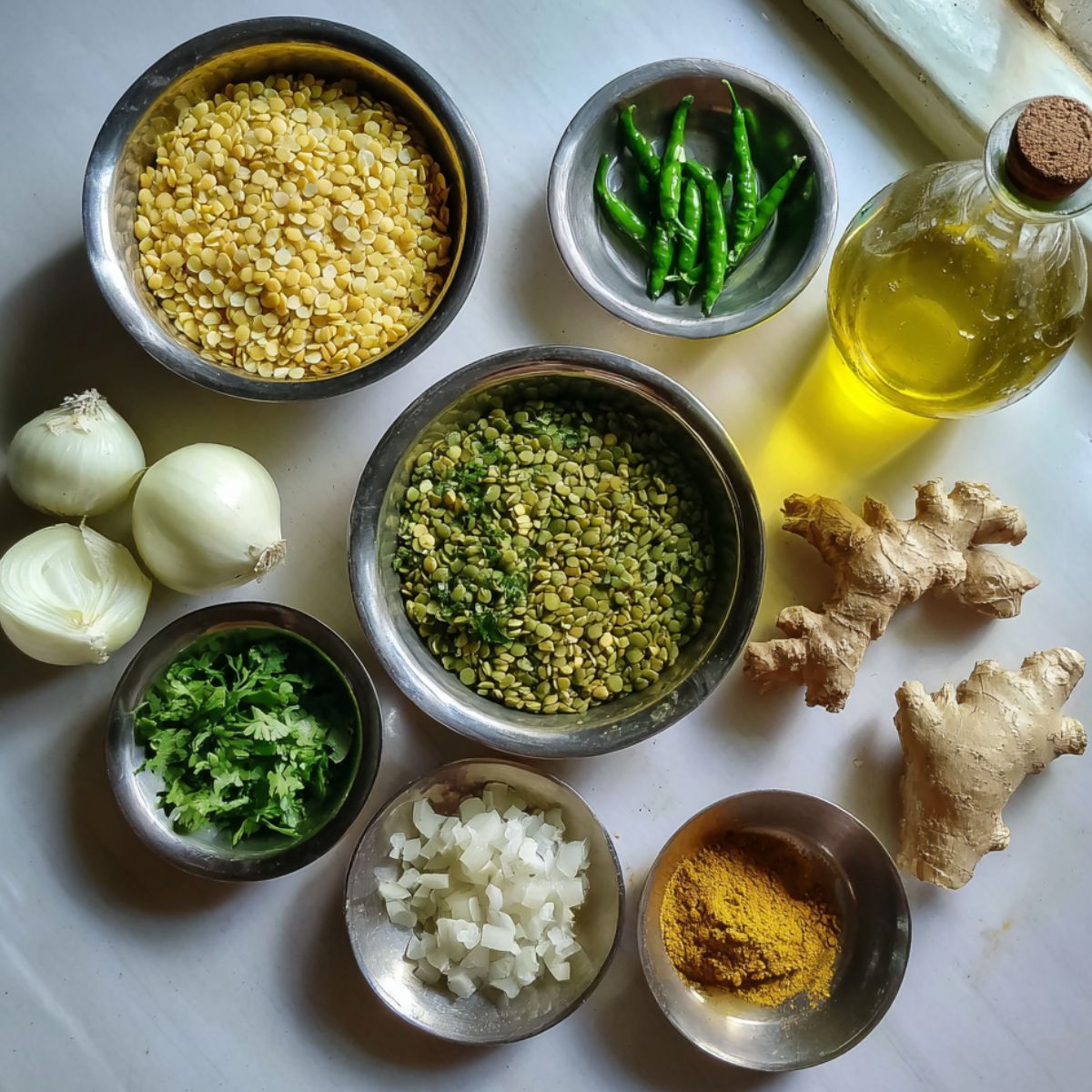Main ingredients for moong dal chilla laid out on a white kitchen counter, top-down casual shot