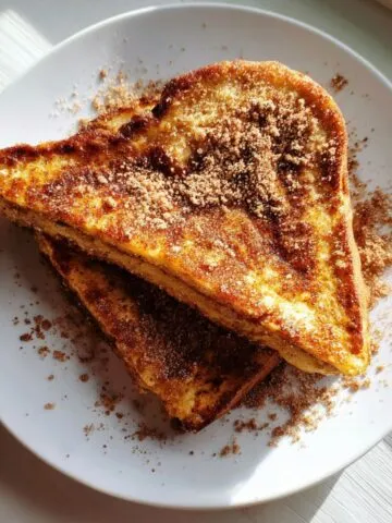 Homemade churro stuffed french toast sprinkled with cinnamon sugar on a white kitchen counter shot from above.