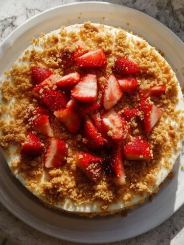 Homemade strawberry crunch cake recipe ; with Oreo crumb topping and strawberries on a white kitchen counter.