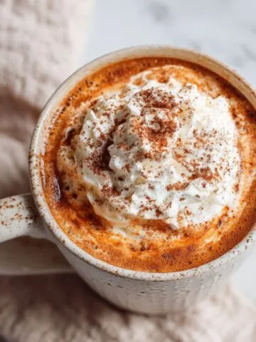Overhead view of homemade pumpkin hot chocolate with whipped cream on a white kitchen countertop