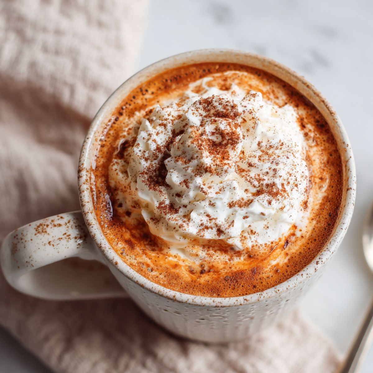 Overhead view of homemade pumpkin hot chocolate with whipped cream on a white kitchen countertop