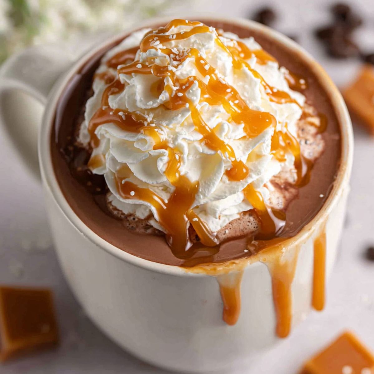 Homemade salted caramel hot chocolate with whipped cream and caramel drizzle on a white kitchen counter shot from above