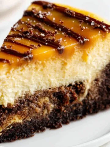A slice of homemade caramel brownie cheesecake with three distinct layers on a white plate