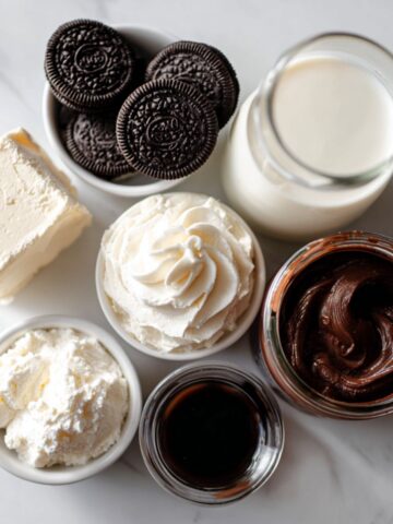 Top view of homemade ingredients for hot chocolate lasagna on a white kitchen counter including Oreo cookies, pudding, cream cheese, and whipped topping
