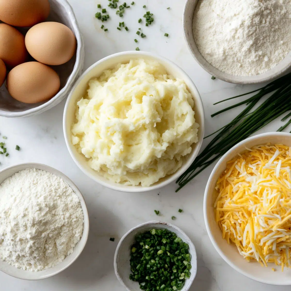Overhead view of ingredients for mashed potato cheese puffs on a white kitchen counter, homemade style