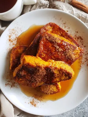 Homemade vegan pumpkin French toast on a white kitchen counter, shot from above with maple syrup drizzled.