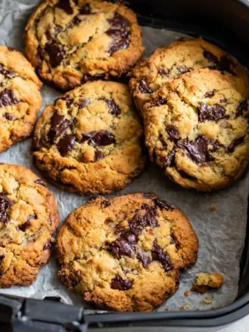 Freshly baked Chocolate Chip Cookies in Air Fryer on parchment paper , imperfectly shaped and golden brown on a white kitchen counter.