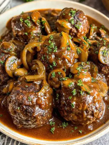 Homemade Salisbury steak meatballs in onion mushroom gravy served over mashed potatoes on a kitchen counter.