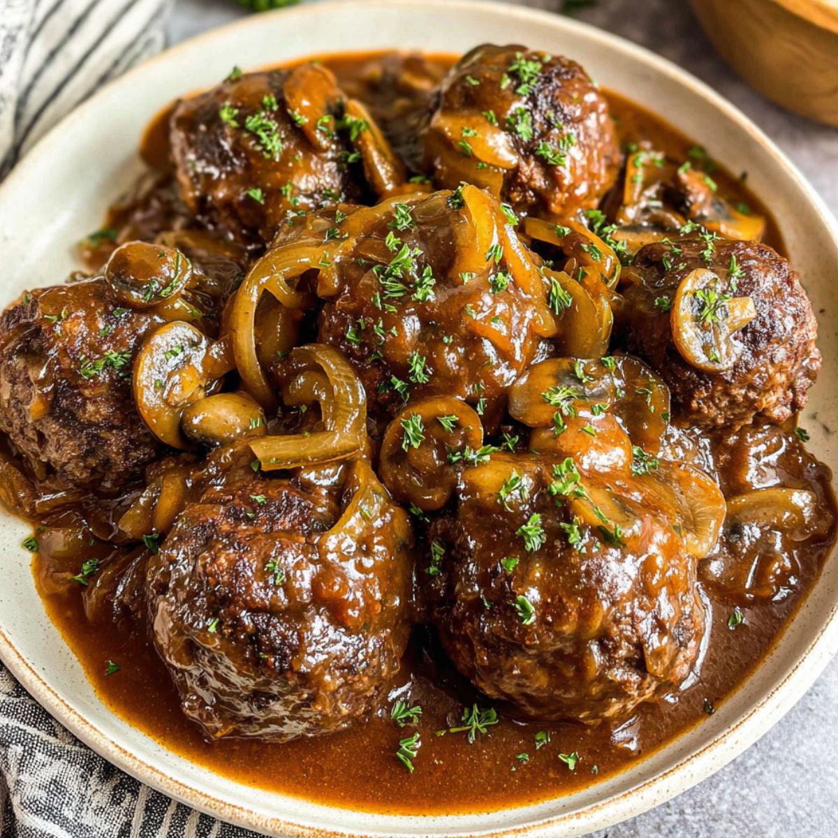 Homemade Salisbury steak meatballs in onion mushroom gravy served over mashed potatoes on a kitchen counter.